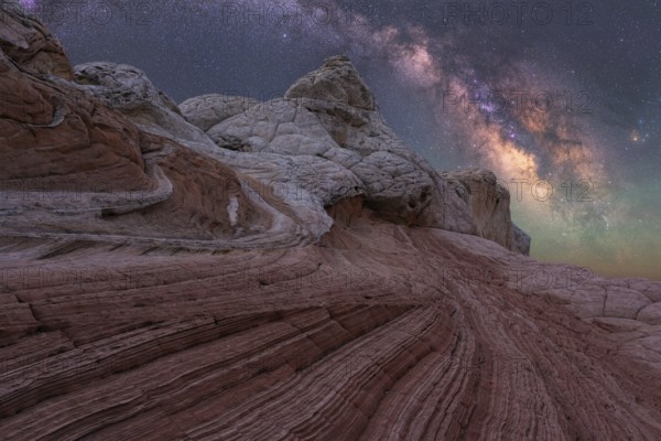Stunning nightscape of White Pocket in Arizona showcases the Milky Way galaxy arching over unique desert rock formations, creating a breathtaking celestial view