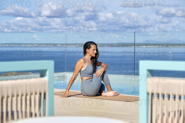 A woman practices yoga on a deck overlooking a vast ocean, enjoying a peaceful environment. The clear sky and tranquil waters create a serene atmosphere