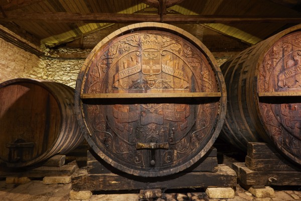 Large wooden barrel with engravings surrounded by stone walls in a wine cellar, Achaia Clauss winery, Patras, Peloponnese, Greece