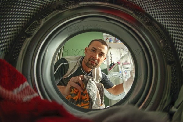 Man loads laundry, looking into washer from inside drum, home chore scene