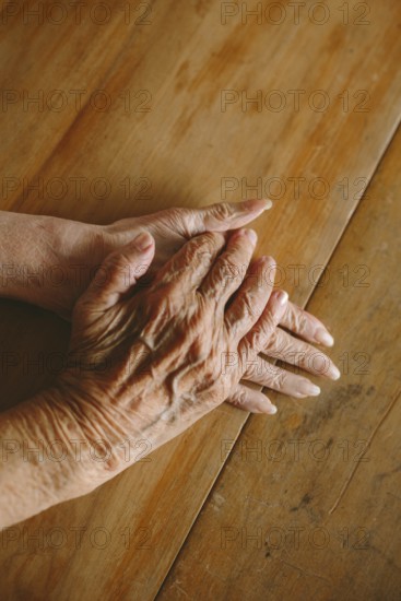 Close-up of elderly hands gently resting on a wooden table, capturing the texture and warmth of aging. Studio lighting enhances the details and shadows