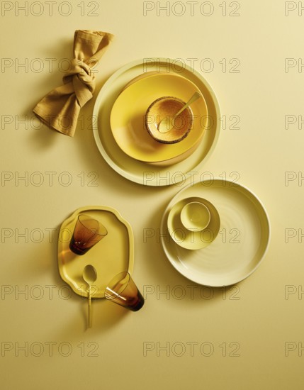 Top view of a stylish yellow ceramic crockery set, including plates, bowls, cups, and a golden napkin, artfully arranged on a yellow surface