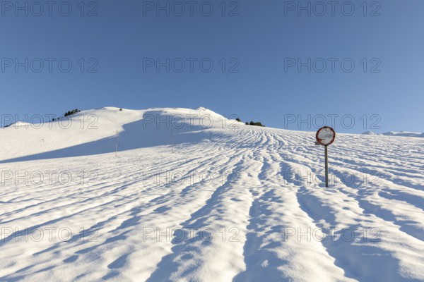 A serene snowy landscape unfolds under a clear blue sky, with a solitary road sign standing amidst the pristine, untouched snow, casting long shadows in the sunlight