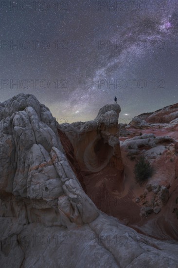 A stunning nightscape of the Milky Way galaxy arching over the unique rock formations at White Pocket in Arizona, US, with a man standing silhouetted against the stars