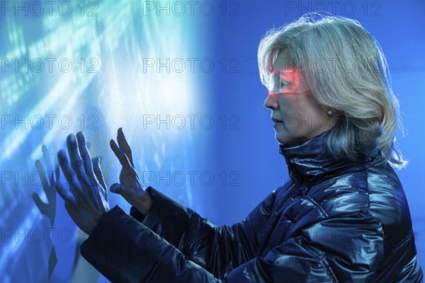 Elderly Asian woman immerses in the metaverse, exploring holographic digital interfaces. Wearing a futuristic jacket, she touches virtual elements, depicting advanced technology use