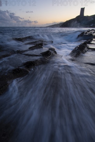 A mesmerizing sunset over the coast of Cadiz in Tarifa. Waves crash onto rocky shores as the sky transitions from day to dusk, creating a serene yet dramatic seascape