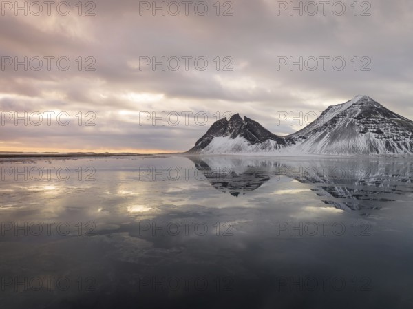 Stokksnes Beach in Iceland showcases stunning winter reflections. Snow-dusted peaks and tranquil waters create a breathtaking landscape, epitomizing Icelandic natural beauty