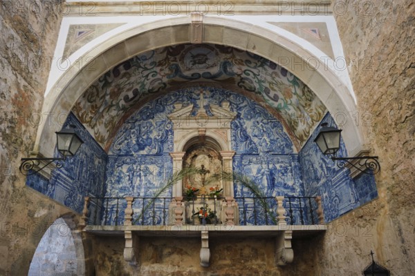 Historic chapel inside Porta da Senhora da Piedade in Obidos, with blue azulejo tiles, painted vault, stone archway and devotional niche in a medieval passage