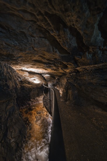 Narrow path in an illuminated cave with flowing water, gloomy adventure atmosphere, Beatus Caves, Switzerland