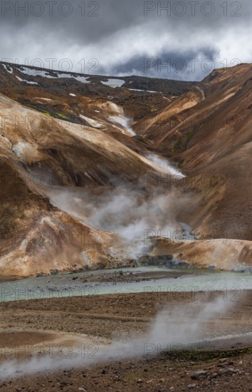 Steaming stream between colourful rhyolite mountains with snowfields, Hveradalir geothermal area, Kerlingarfjöll, Icelandic highlands, Iceland