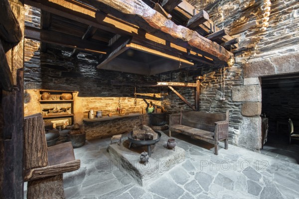 Traditional rustic kitchen inside a country house in Lugo, Spain, featuring stone walls, wooden beams, and antique utensils