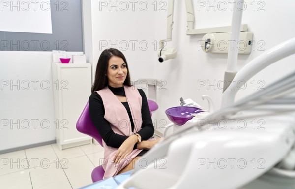 A patient in a modern dental clinic awaits her checkup, sitting in a comfortable chair. The clinic features advanced dental equipment, creating a welcoming and professional environment