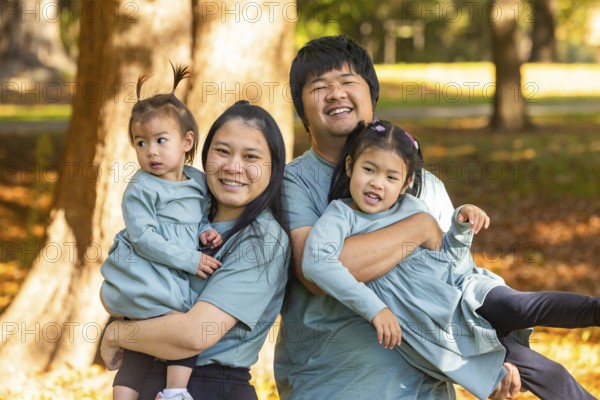 A joyful Asian family with parents and two young children, smiling and playing together in a sunny park. The warm atmosphere emphasizes love and togetherness in nature
