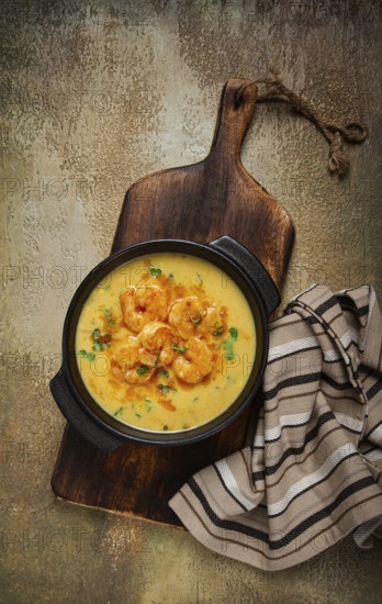 Creamy shrimp curry with spices, garnished with herbs, on a textured background, homemade, no people