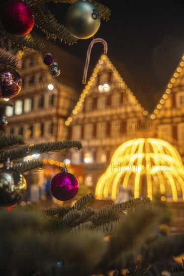 Close-up of Christmas baubles on a tree in front of a glowing structure and houses, Christmas market Calw, Black Forest, Germany