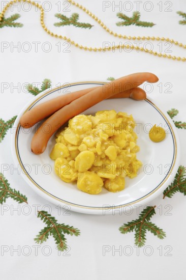Swabian cuisine, potato salad with string sausages, Wienerle, Wiener sausages, thin boiled sausage, horseradish sausage, Frankfurter sausage, savoury, salty, typical Swabian, typical Christmas dinner, quick cuisine for Christmas Eve, home cooking, plate, mustard, Christmas decoration, golden chain on the back, hand-embroidered table linen, Christmas motifs, fir branch motif, Christmas tablecloth, handmade, traditional cuisine, food photography, studio, Germany