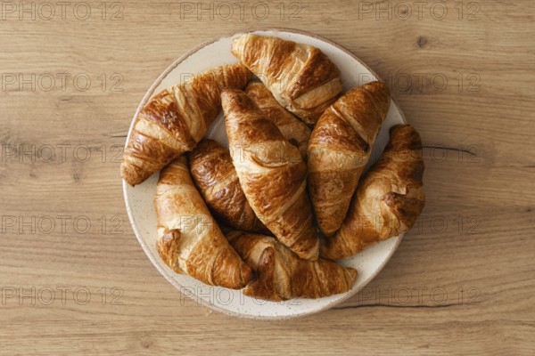 A top view of freshly baked homemade croissants arranged on a white plate, placed on a wooden surface. The golden brown pastries evoke a warm, inviting atmosphere