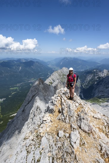 Mountaineer with helmet on a mountain ridge, ascent to the Zugspitze, Zugspitze via ferrata, mountain landscape, view of Eibsee lake and mountain ridge with summit Waxenstein and Riffelspitze, Wetterstein range, Wetterstein range, Bavaria, Germany