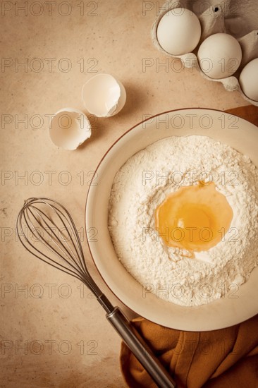 Food background, concept, plate with wheat flour, broken egg, whisk, kitchen towel, on a beige table, top view, rustic