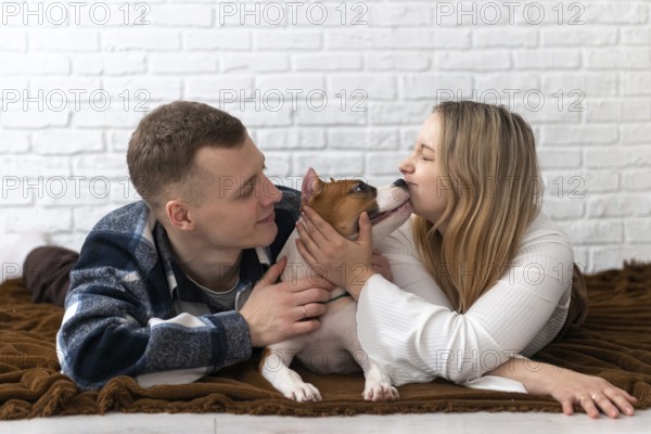 A young man and woman lovingly interact with their Staffordshire Terrier puppy dog at home, creating a heartfelt scene in a cozy setting with a white brick background