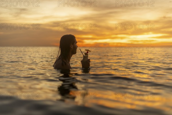 Silhouette of man relaxing in the ocean at sunset, holding a cocktail, enjoying a serene vacation moment in the Philippines