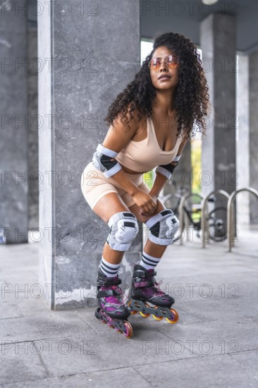 Vertical photo of an urban latin woman posing with inline skates and pink sportive clothes in an urban park