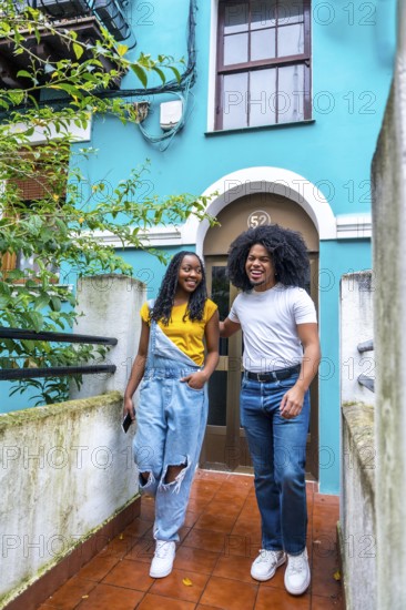 Vertical photo with copy space of a young casual african couple leaving a blue colorful house