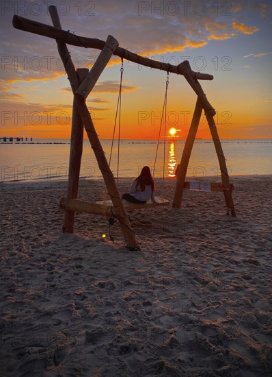 Young girl sitting on a swing on the beach watching sunrise on the island of Rügen, Mecklenburg-Western Pomerania, Germany