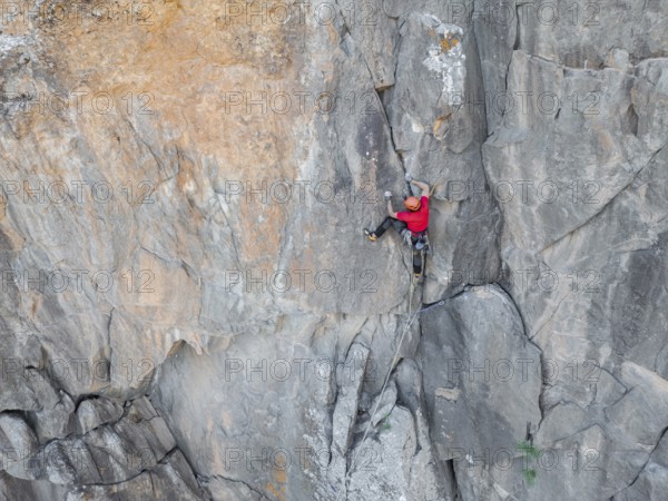 A climber skillfully ascends a rugged cliff face, showcasing traditional climbing techniques amidst a stunning natural landscape. The scene captures adventure and courage