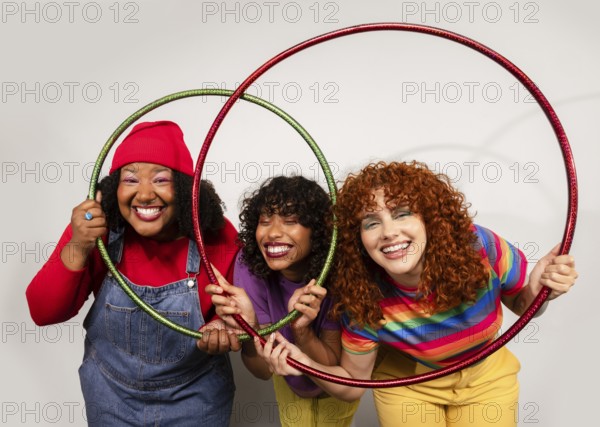 Three women share joyful moments, smiling brightly as they play together with colorful hula hoops. Their cheerful expressions and vibrant outfits create a lively scene