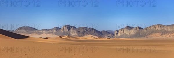 Gentle sand dunes with mountains in the background and a bright blue sky, The landscape of the Sahara in Algeria