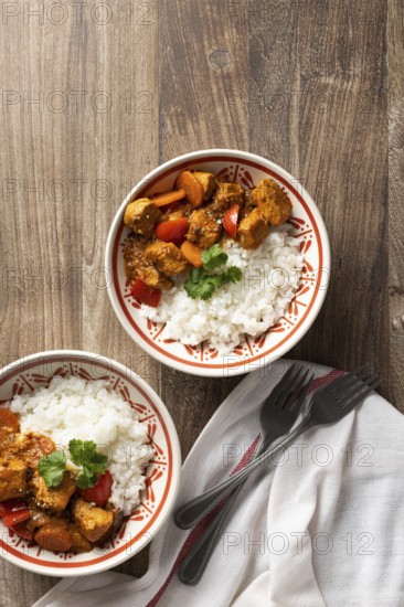 Top view of two bowls of flavorful Hungarian pork goulash with rice, served on a wooden table. The bowls are adorned with cilantro and feature tender pork, rice, and bell peppers