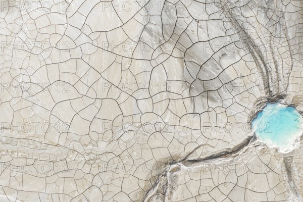 Aerial view of cracked earth with intricate lines and a vibrant blue water body in the corner. This striking natural pattern contrasts the arid and aquatic elements