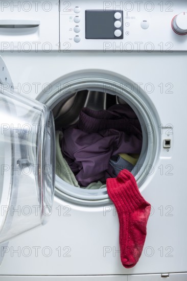 A bright red sock hangs from the door of an open front-load washing machine filled with laundry, emphasizing a humorous and relatable laundry moment at home