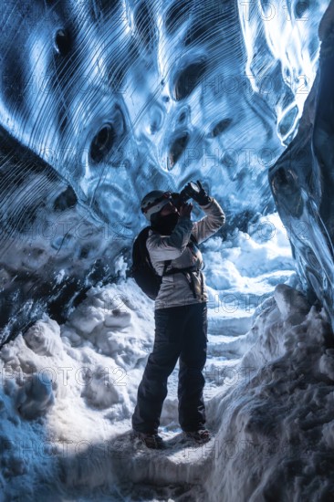 A person is taking a picture in a cave with a backpack on. The cave is filled with ice and snow