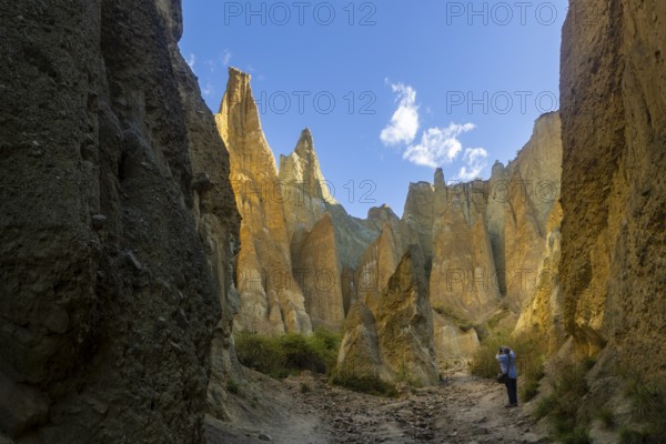 Back view of unrecognizable person exploring the dramatic Clay Cliffs in the Canterbury region of New Zealand, capturing their striking geology under a vibrant sky