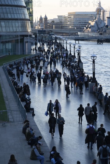 People walking next to the River Thames as evening falls, The Queen's Walk, Southwark, London, England, UK