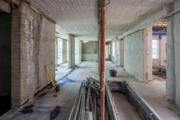 Unfinished building interior showcases raw concrete walls, scattered tools, and construction materials. Sunlight filters through windows, highlighting ongoing transformation