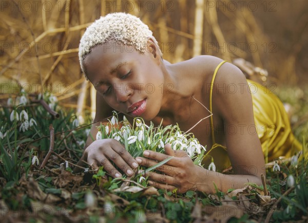 A woman in a golden dress lies peacefully among blossoming snowdrops, enjoying nature tranquility in Tacony Creek Park. Her serene expression reflects a deep connection to the natural world