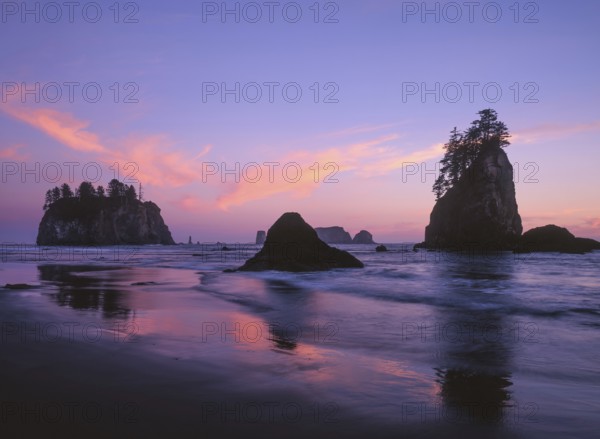 The sky glows in shades of pink and purple as the sun sets over Second Beach, with sea stacks rising from the Pacific Ocean and their reflections shimmering on the wet sand