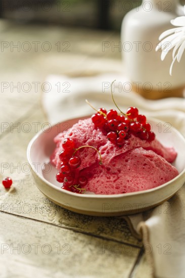 Homemade pink berry mousse garnished with fresh red currants in a ceramic bowl on a tiled table, creating a vibrant food scape