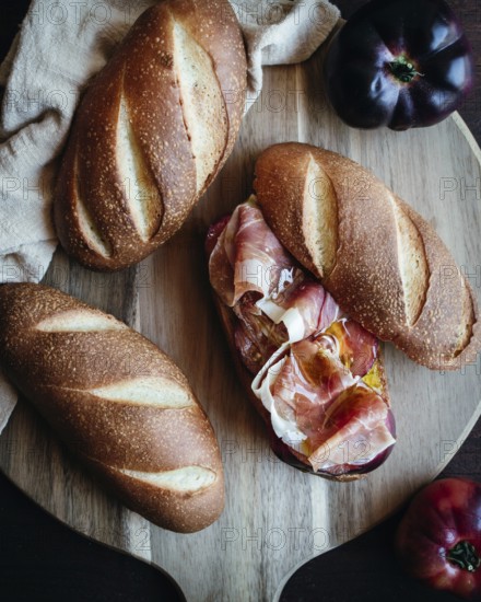 Freshly baked olive oil bread topped with slices of serrano ham and ripe tomatoes on a rustic wooden board, showcasing a delicious Mediterranean snack ready to enjoy