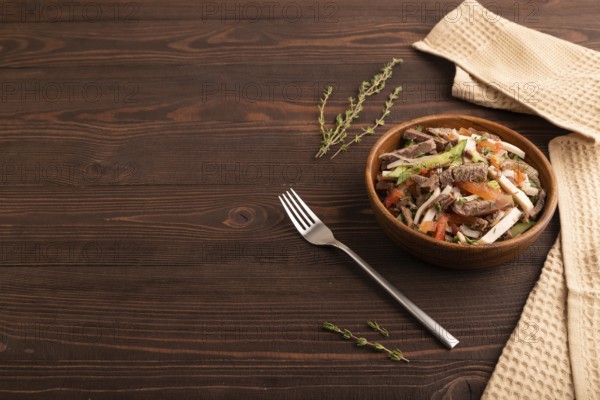 Meat salad with beef and vegetables in wooden bowl on brown wooden background and linen textile. side view, copy space
