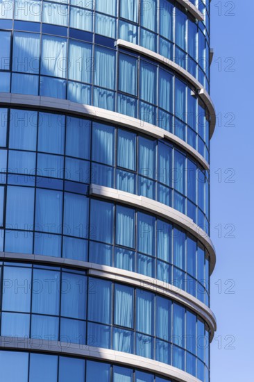 Modern architecture, highlighting a curved building with a vibrant blue glass facade against a clear sky. The structure features elements of concrete, glass, and metal, emphasizing contemporary architectural design and urban aesthetics