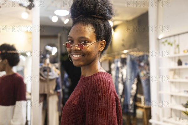 An elegant woman with curly hair tries on a pair of distinctive sunglasses in a fashion store. She smiles confidently, showing off her personal style and the design of the glasses