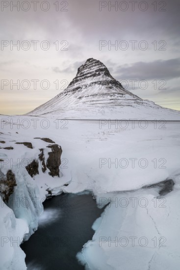 Kirkjufell Mountain, Iceland's iconic landmark, surrounded by a snowy landscape and icy waters, captures the serene beauty of winter in Iceland's natural scenery