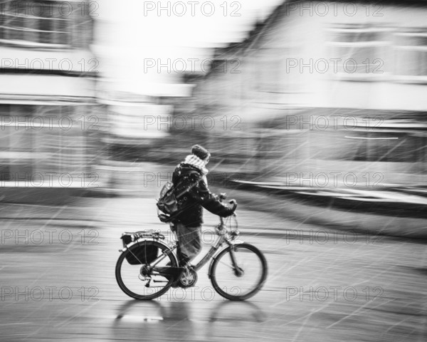 A person on a bicycle rides through a city in bad weather and sleet, rainy day black and white photograph, Baden-Württemberg, Germany
