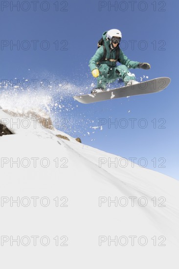 A snowboarder expertly navigates a thrilling freeride descent, capturing the essence of extreme sports in a pristine winter setting. The crisp, clear blue sky frames this exhilarating moment