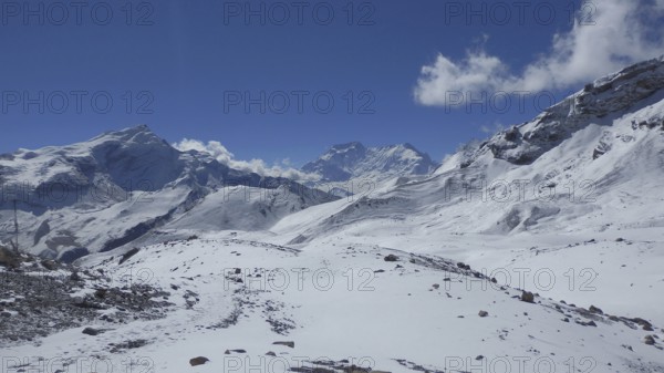 Clouds move across snowy mountain scenery on the way to Thorong La Pass, with rugged peaks and blue skies, trekking at Annapurna Circuit, Manang, Nepal