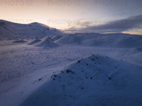 A serene winter twilight spreads over snow-draped hills in Iceland, capturing the tranquil beauty and ethereal glow of the frosty landscape under a pastel sky